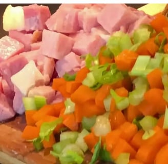 Cubed ham with chopped carrots and celery on a cutting board by the pot