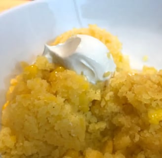 Mexican Corn Cake in white bowl with dollop of sour cream and corn kernals scattered in bowl.