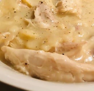A bowl of old-fashioned Southern chicken and dumplings served in a white bowl with orange spray floral in the background.
