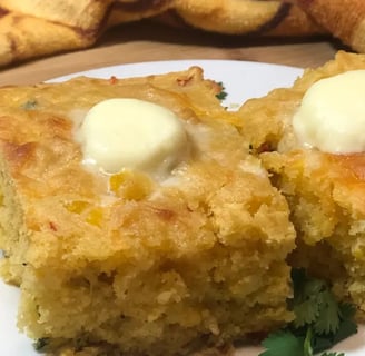 Two blocks of Mexican cornbread topped with pats of melting butter on a rustic plate