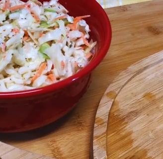 Creamy tangy and sweet coleslaw in a red bowl beside a pulled chicken sandwich on a plate.