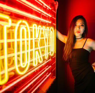 a woman in a black dress standing in front of a neon sign that says Tokyo