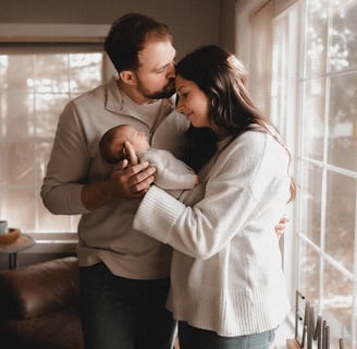 Mom and dad standing by their window with their newborn