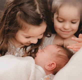 Two sisters holding new baby brother and feeling baby's hair