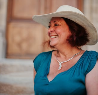 Portrait de Flo Salort assise sur des marches, sourire et chapeau, incarnant liberté et féminité