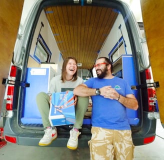 a man and woman standing in a van with surfboards