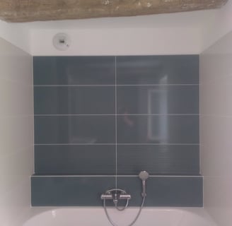 Grande baignoire avec faïences bleu/vert en fond et des retours en beige