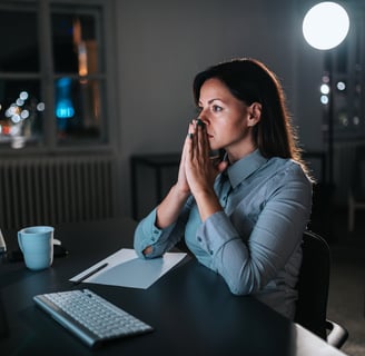 Mulher sentada na frente do computador com as mão juntas a frente do rosto preocupada