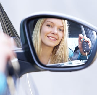 a woman is holding a keychain and looking in the mirror after passing her driving test 1st time