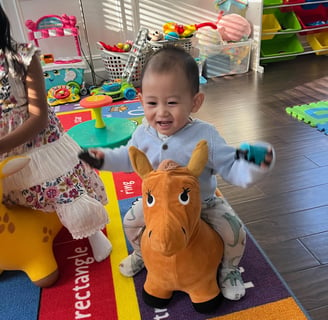 Photo of young child laughing while playing on a toy horse.