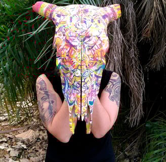 peinture aux couleurs vives sur un crane tenu par l'artiste comme un masque
