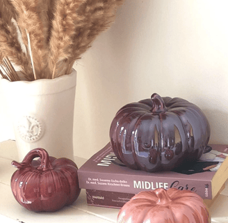 a vase with dried wheat and three purple ceramic pumpkins