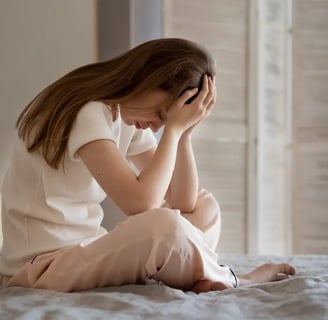 a woman sitting on a bed with her hands on her head