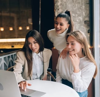 three girls sitting at a table with a laptop