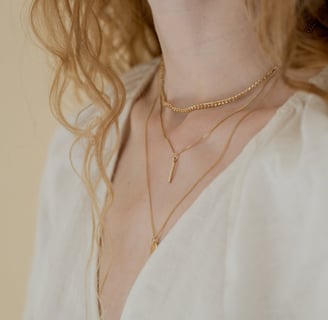 Foto do pescoço de uma mulher utilizando três colares diferentes em dourado.