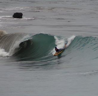 A bodyboarder riding a wave and another surfer watching from the water