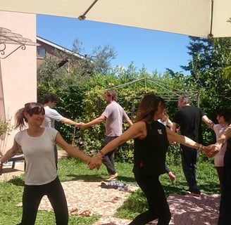 a group of people holding hands and dancing in a garden, classe di bioenergetica