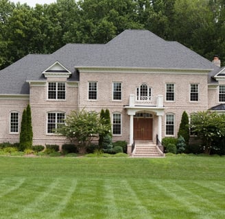 Large stately tan brick home on private lot with lush green grass in Virginia