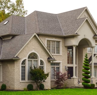 A stately tan brick house with beautiful landscaping and shrubery