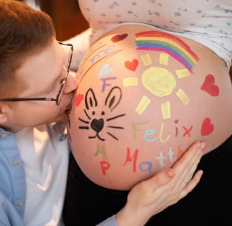 werdender Vater küsst bemalten Babybauch seiner schwangeren Frau