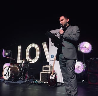 Alex hosting an awards event in front of giant letters spelling LOVE