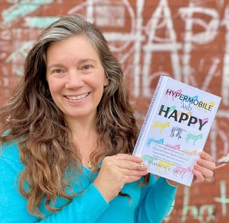 pretty woman with long brown hair in a turquoise sweater holding a book in front of a brick wall