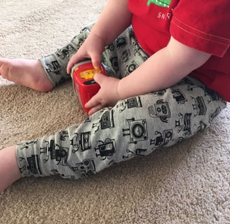 a toddler boy sitting on the floor with a toy wearing robot music robot themed leggings