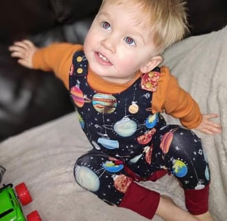 a baby boy wearing a christmas grow with me romper in space bauble fabric
