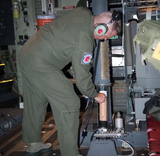 USAF personel loading a dropsonde into chamber that will shortly release it from moving aircraft.