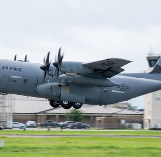 US Air Force Hurricane Hunter plane taking off with ground just below plane and control tower in back ground.