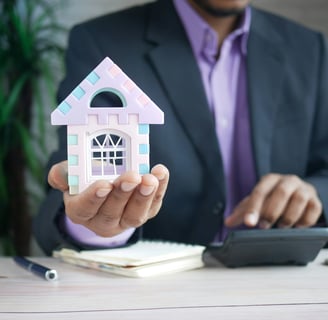 man holding a model house in his hand and calculator. Photo by Towfiqu barbhuiya on Unsplash