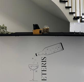 Stilingas baltas baro stalas su minimalistiniu užrašu „ETERIS“, dekoruotas grafiniu butelio ir taurė