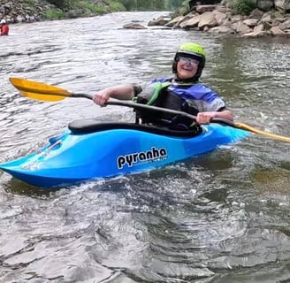 Women in a playboat (freestyle kayak) holding a paddle, Wearing helmet and BA  smiling. 