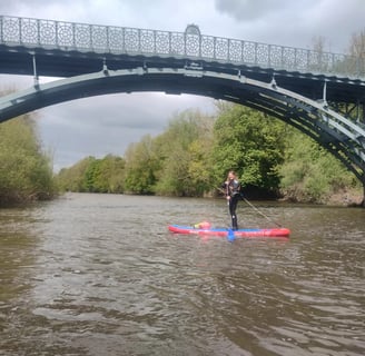 a women standing on a paddle board on the river severn under a bridge, 
