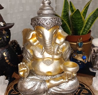 La foto muestra una figura decorativa de Ganesha en colores plata y oro