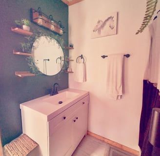 a bathroom with a round mirror and wooden shelves and black hardware hunter green and white