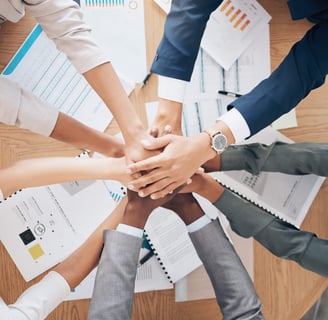 group of business people stacking hands over a table covered with charts and graphs