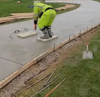 a sidewalk of wet concrete being leveled by a worker that is wearing personal protective gear.