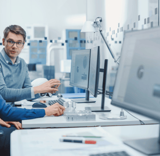 a man and woman sitting at a desk with a computer monitor