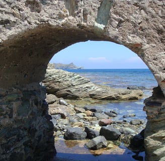 Arcade rocheuse en forme de rond par lequel on aperçoit des rochers et la mer toute bleue