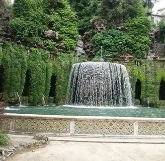 Cascade se jetant dans 1 bassin et entourée de plantes tombantes et de colonnes