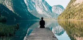 Homme de dos assis sur un ponton face à un lac ecaissé entre deux montagnes