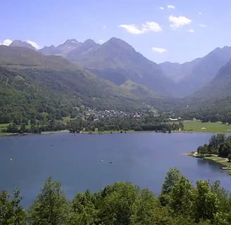 Lac bordé de bois en premier plan et village de Genos en arrière plan au pied des montagnes