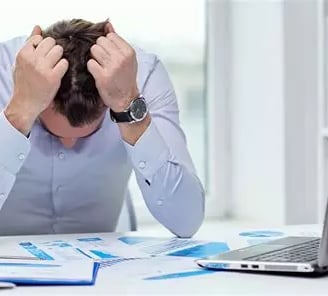 Homme stressé tête baissée avec coudes sur son bureau et ses deux mains sur sa tête
