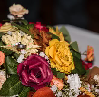 Beautiful bouquet of paper roses custom made with text quote on the flowers with the couples wedding rings resting on top