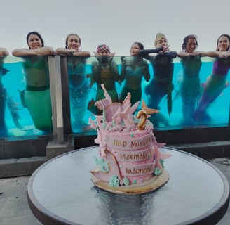 a birthday cake in ocean mermaid theme and the celebrating mermaids in the background, swimming in a