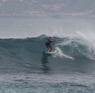 Romi riding a wave while surfing at Ekas beach, showcasing his skills as an experienced instructor.