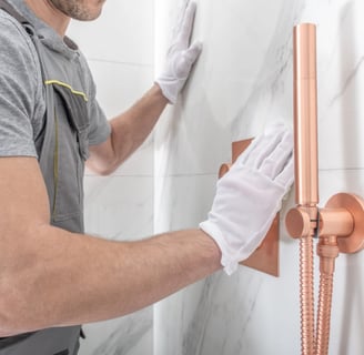 a hanndyman in a grey shirt and gloves is holding a shower head in Vancouver