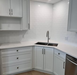 Corner sink area with white shaker kitchen cabinets, quartz countertop, subway tile backsplash, and 