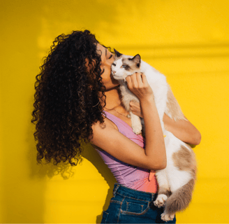 a woman holding a cat that is sitting on a yellow wall